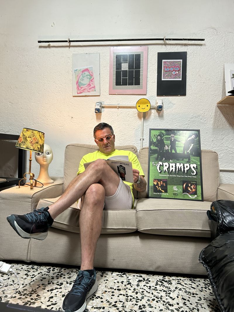 Bert leyendo un libro de Issey Miyake en un sofá, junto a un póster de The Cramps